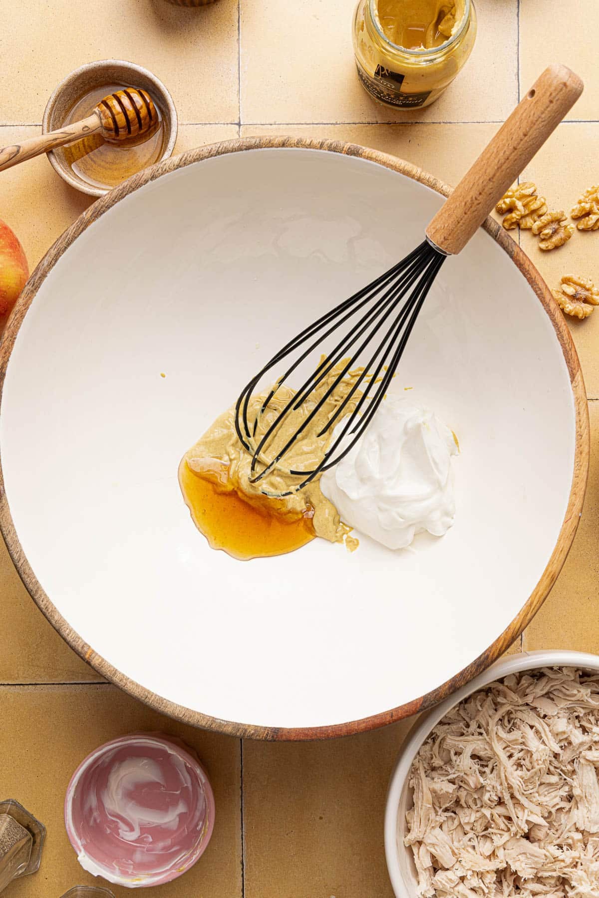 All of the ingredients for the honey mustard dressing in a white bowl with a whisk before whisking.
