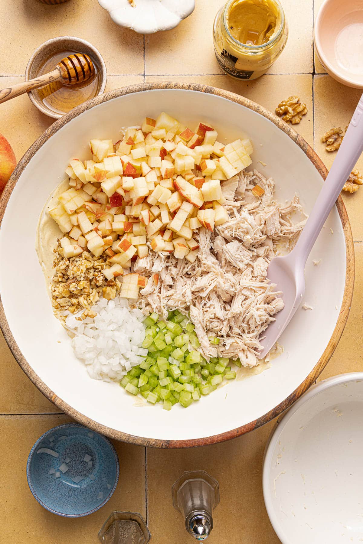 The chopped chicken, celery, onion, apple, and walnuts in the bowl with the dressing before mixing everything together.