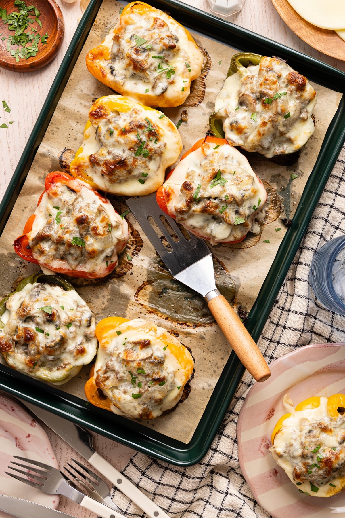 A spatula sits on the baking sheet with the philly cheesesteak stuffed peppers after baking. One pepper is missing from the sheet pan.