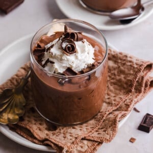 A jar of high protein chocolate pudding on a countertop garnished with whipped cream and chocolate shavings.