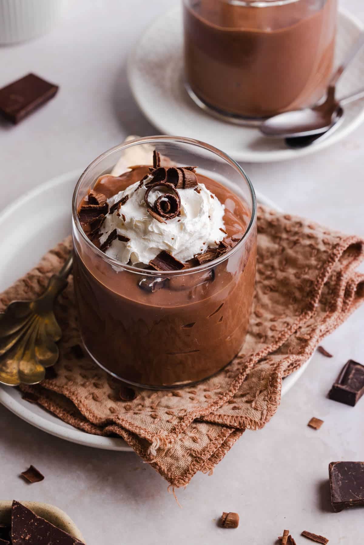 A jar of high protein chocolate pudding on a countertop garnished with whipped cream and chocolate shavings.