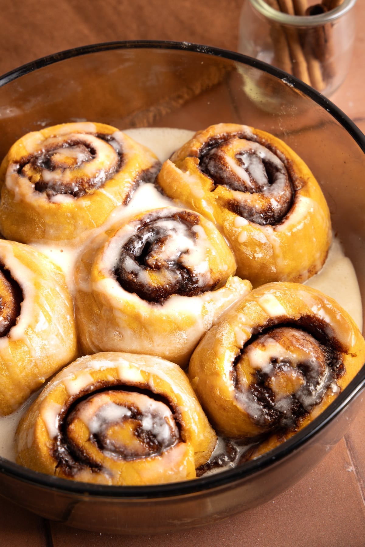 Six pumpkin cinnamon rolls in a baking dish with the glaze on top.