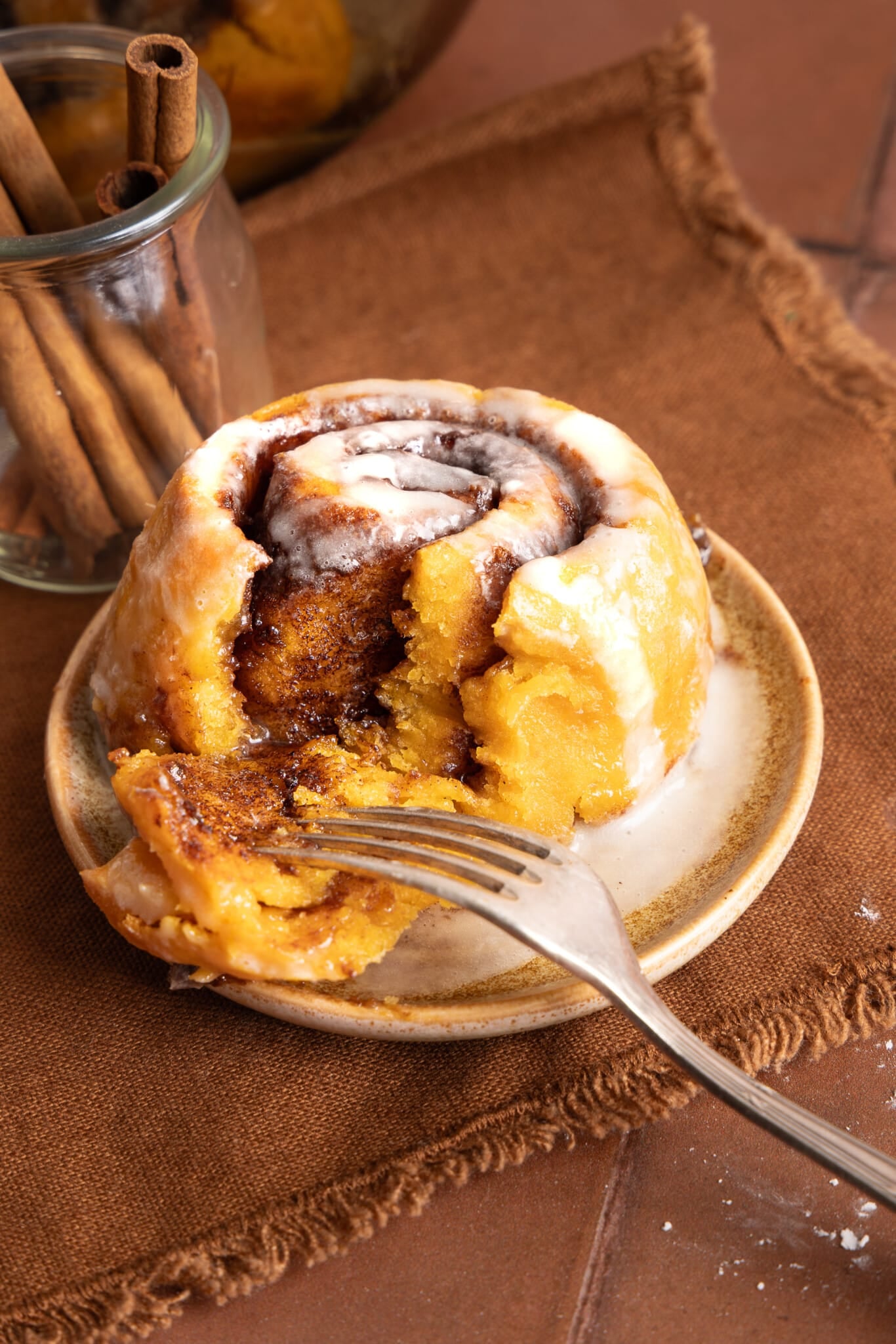 A pumpkin cinnamon roll on a plate with a fork.
