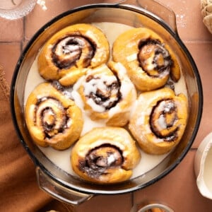 Six baked pumpkin cinnamon rolls in a baking dish with the glaze drizzled over the top.