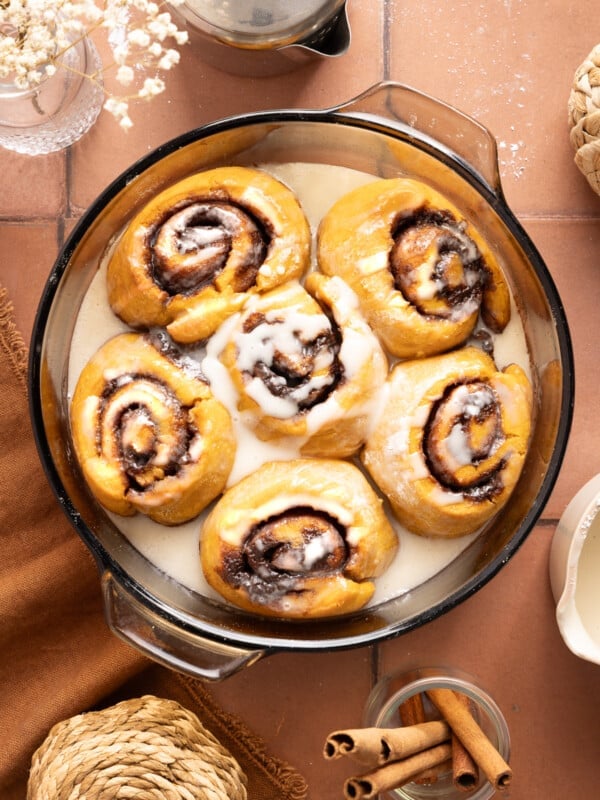 Six baked pumpkin cinnamon rolls in a baking dish with the glaze drizzled over the top.