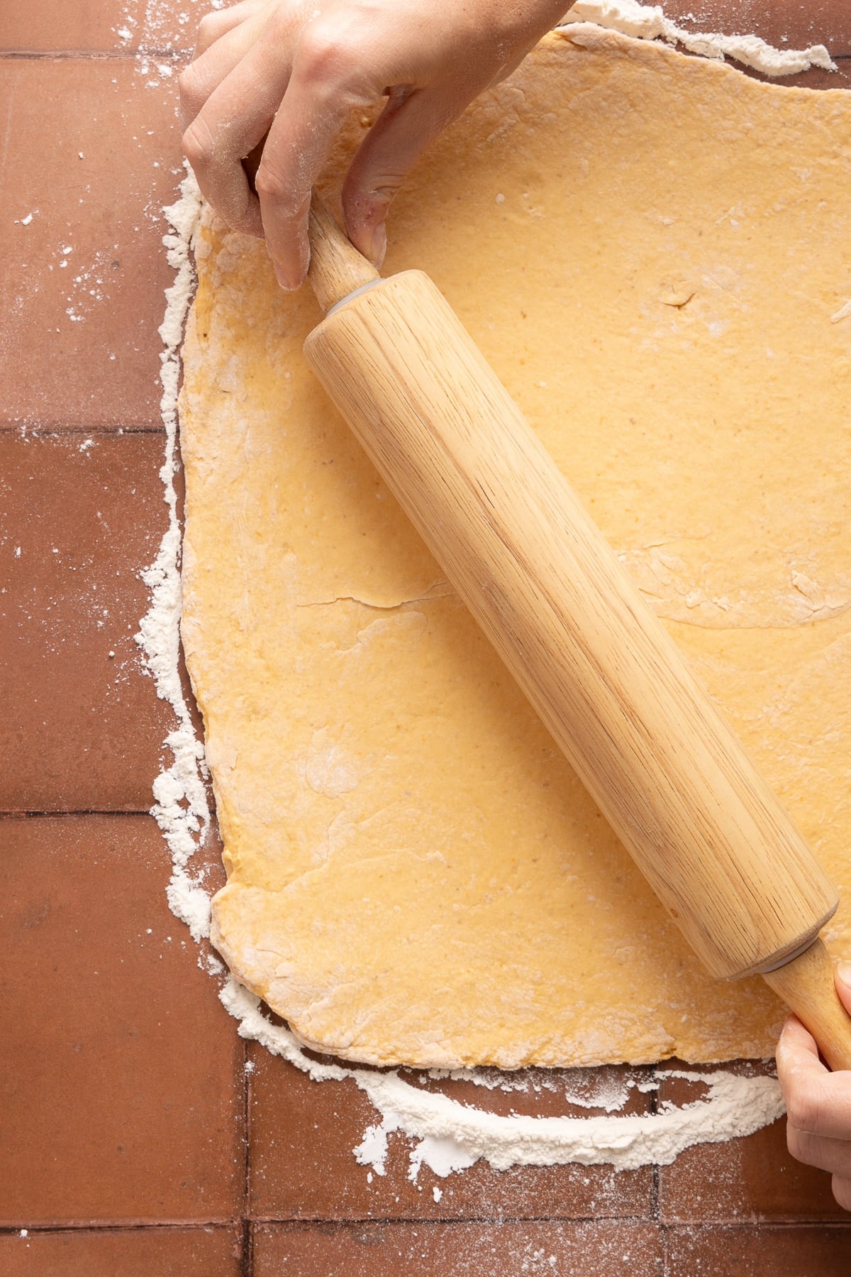 A rolling pin rolls the dough into a rectangle on a floured surface.