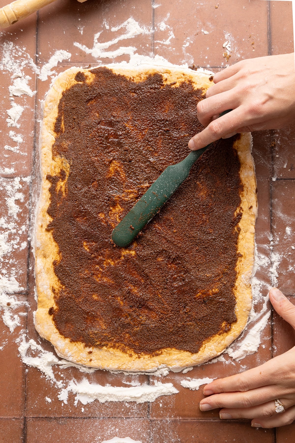 A spatula spreads the cinnamon sugar mixture over the rolled out dough.