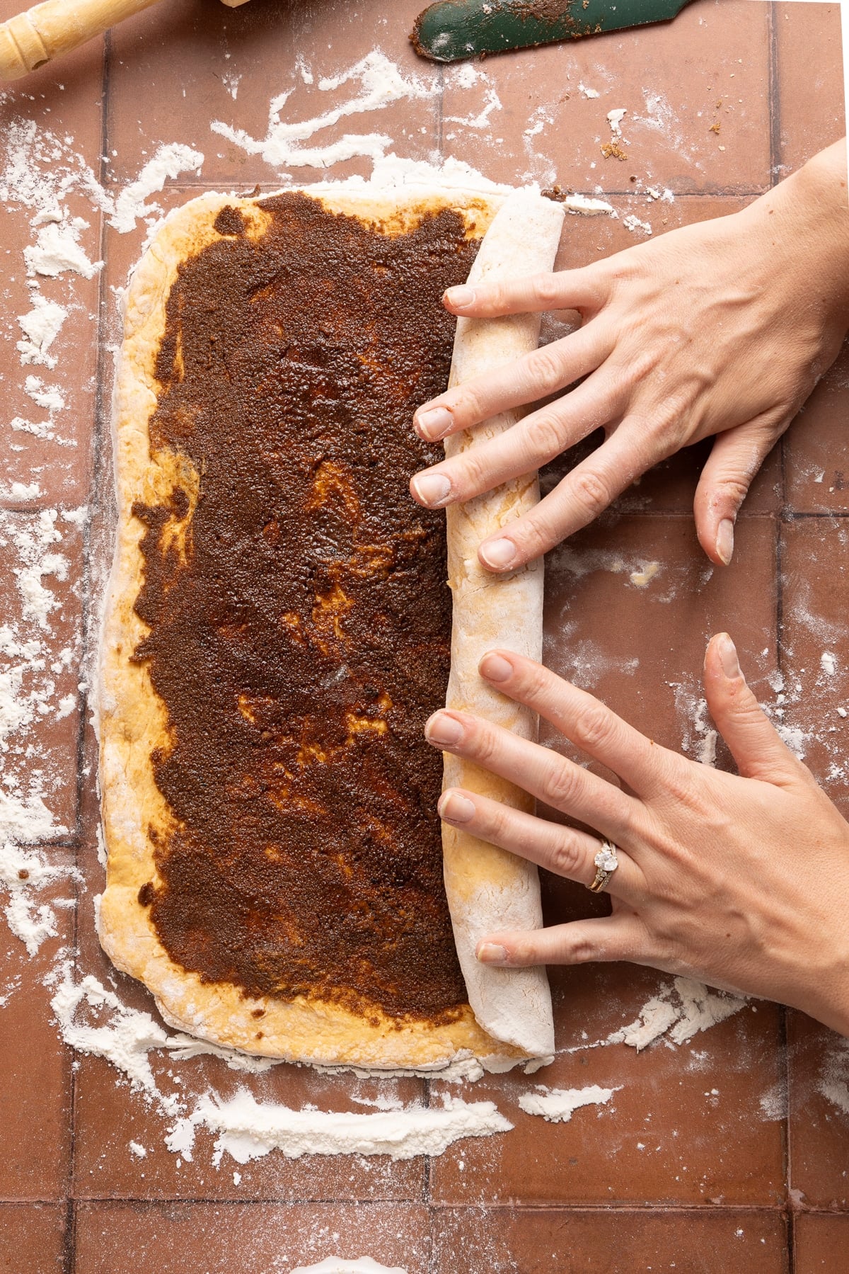 Two hands roll the dough up into a large log before slicing into cinnamon rolls.