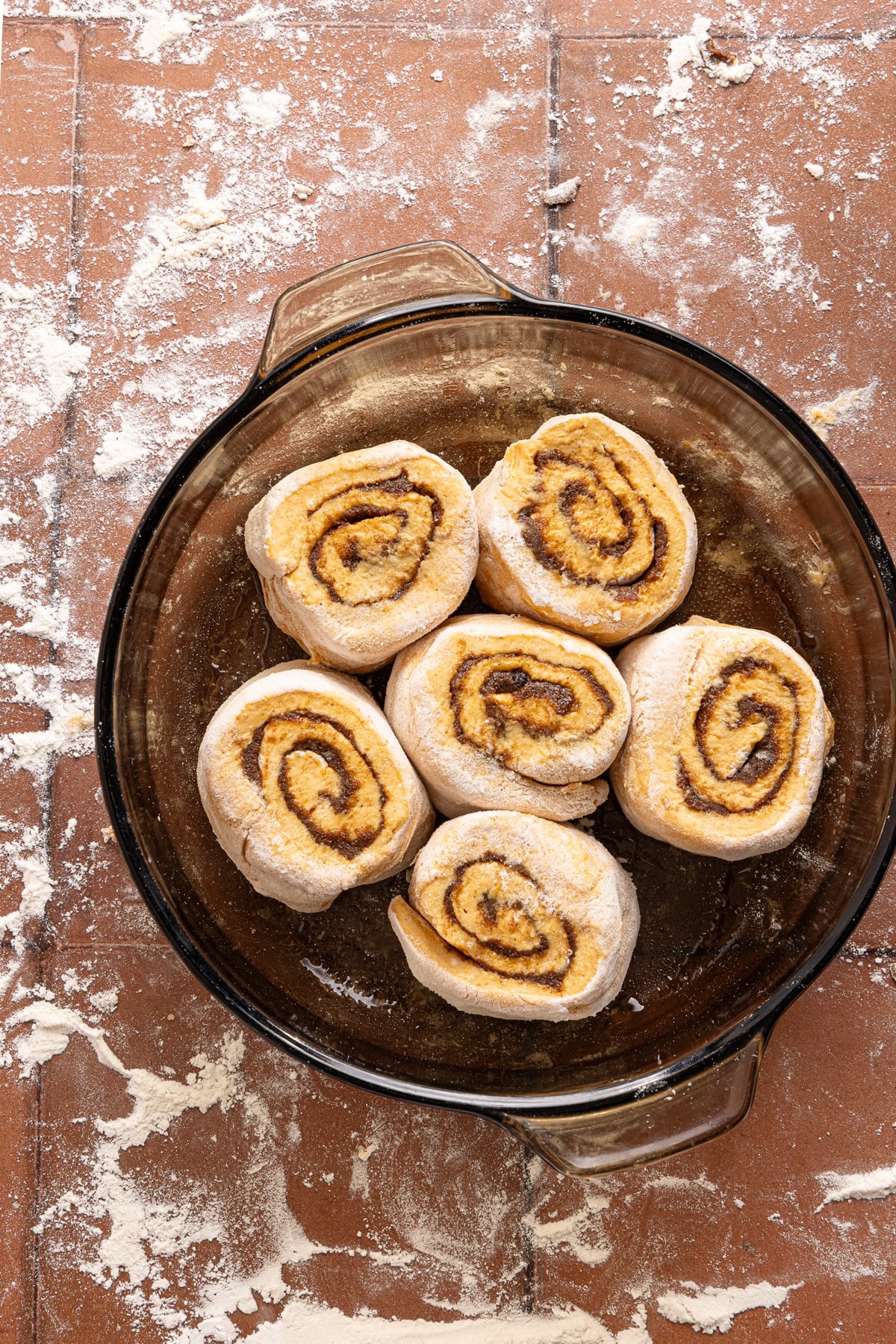 Six pumpkin cinnamon rolls in a glass baking dish on a countertop.
