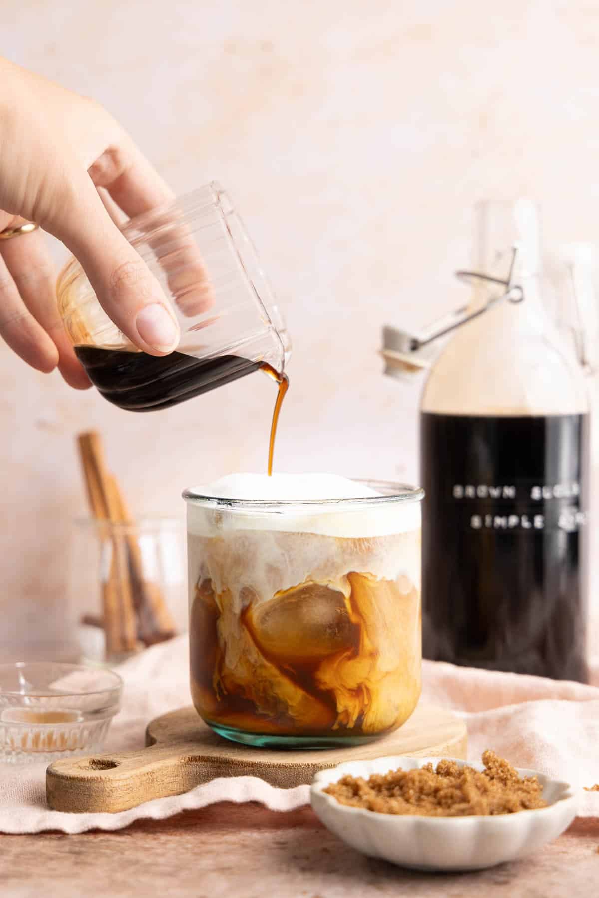 A glass pouring the brown sugar syrup into an iced coffee.