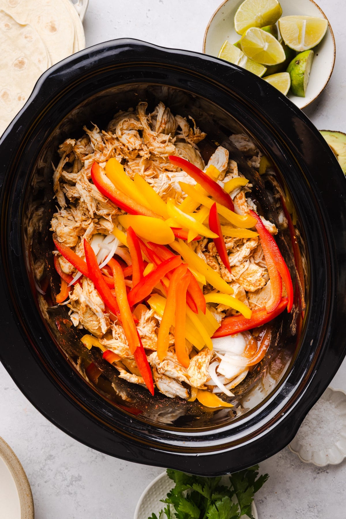 The shredded cooked chicken and raw. bell peppers in the slow cooker before softening the peppers.