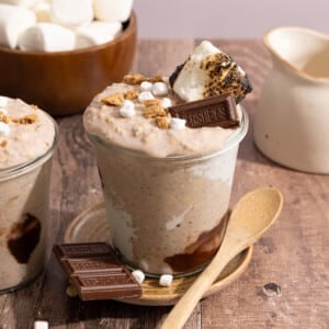 A glass jar container of s'mores overnight oats on a countertop with marshmallow, chocolate, graham crackers, and toasted marshmallow topping.