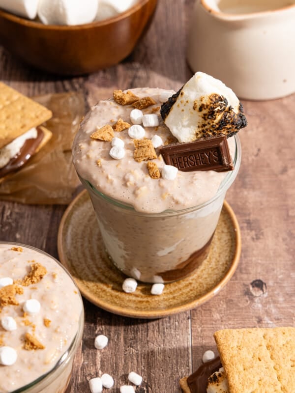 S'mores overnight oats in a glass jar with mini marshmallows, crushed graham crackers, a piece of hershey's chocolate bar, and a toasted marshmallow on top.