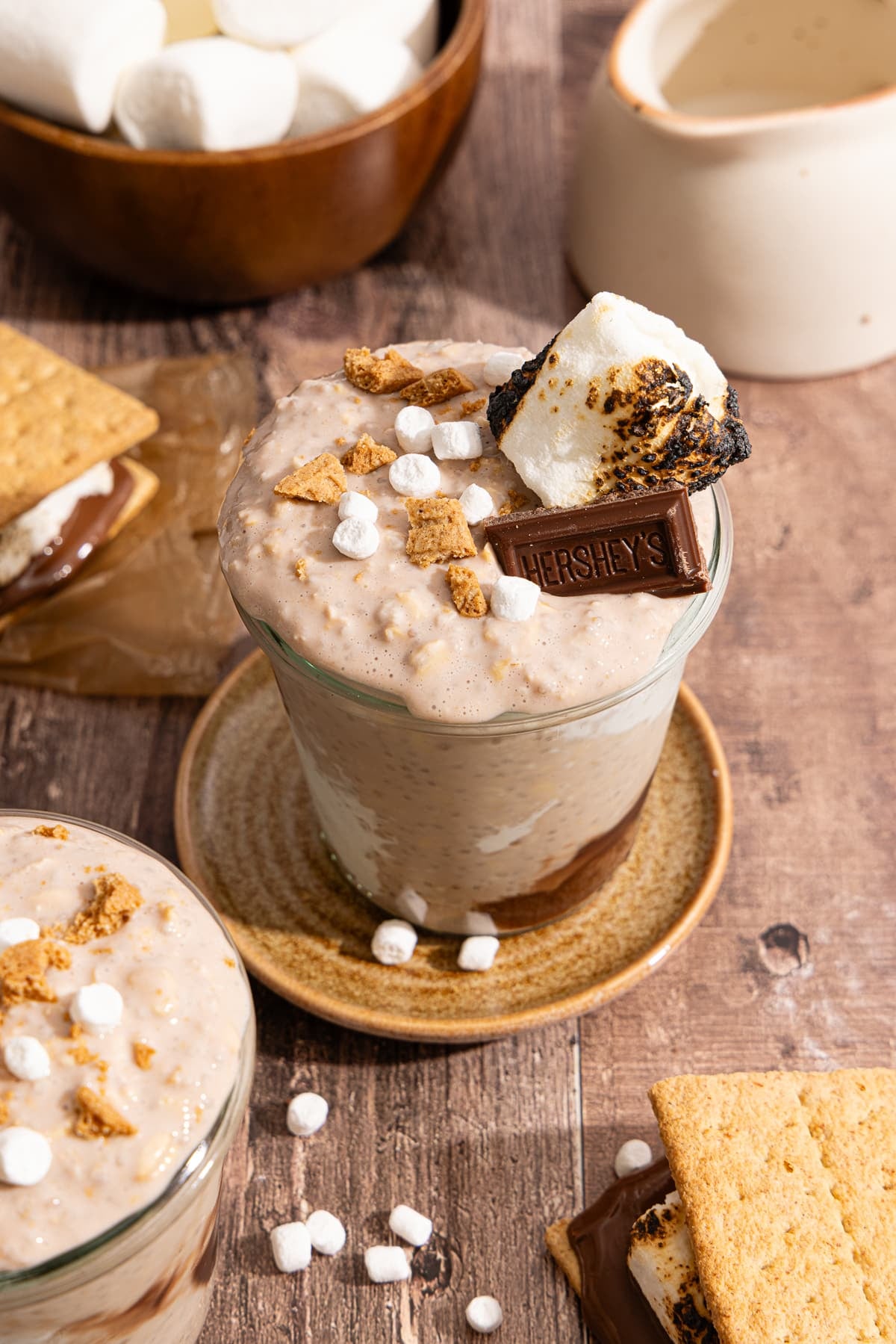 S'mores overnight oats in a glass jar with mini marshmallows, crushed graham crackers, a piece of hershey's chocolate bar, and a toasted marshmallow on top.