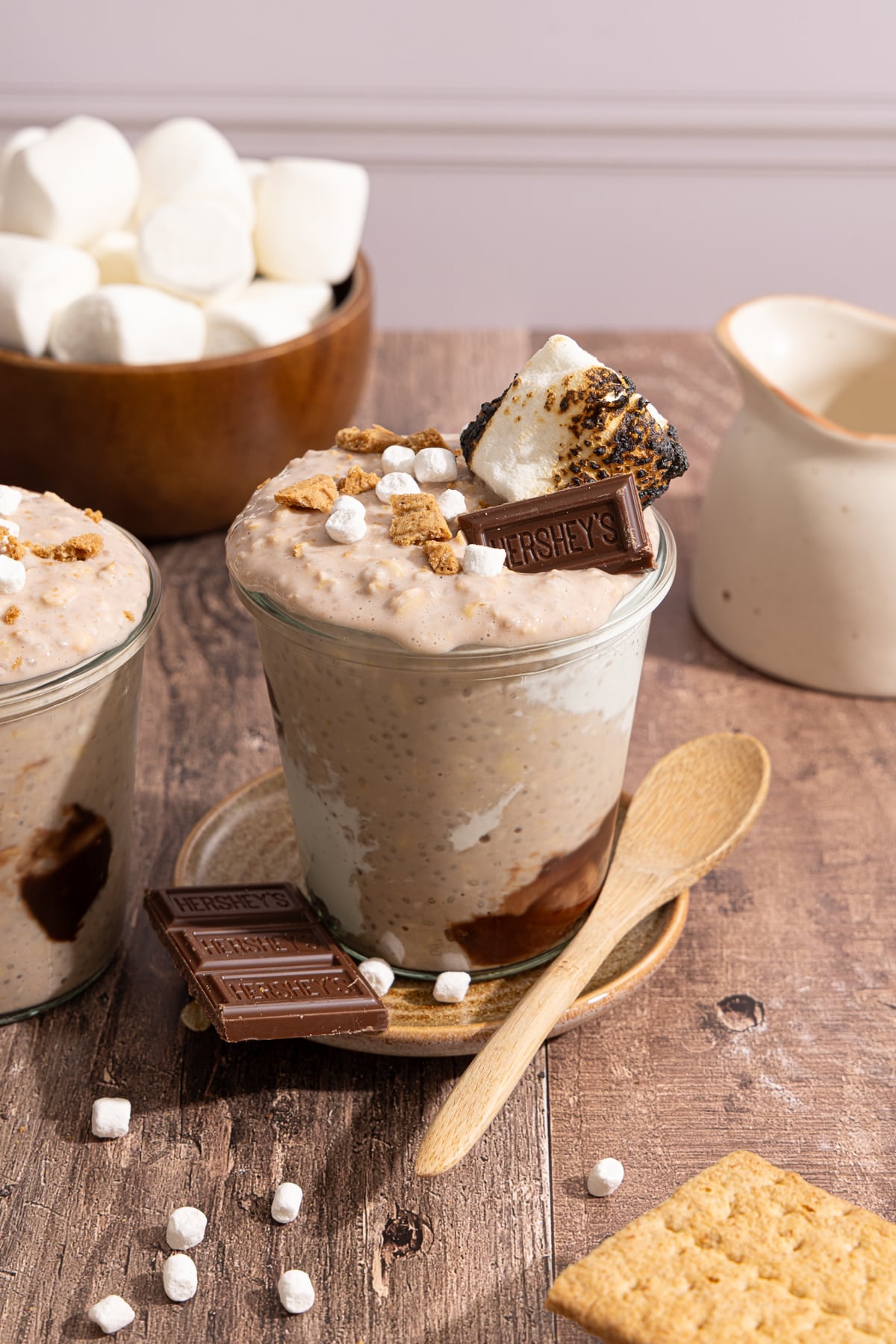 A glass jar container of s'mores overnight oats on a countertop with marshmallow, chocolate, graham crackers, and toasted marshmallow topping.
