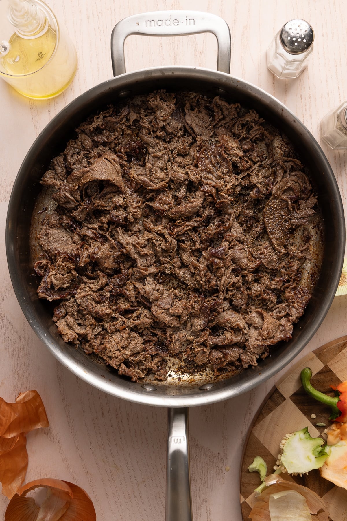 The shaved steak, salt, pepper, and worcestershire sauce cooking in a large skillet.