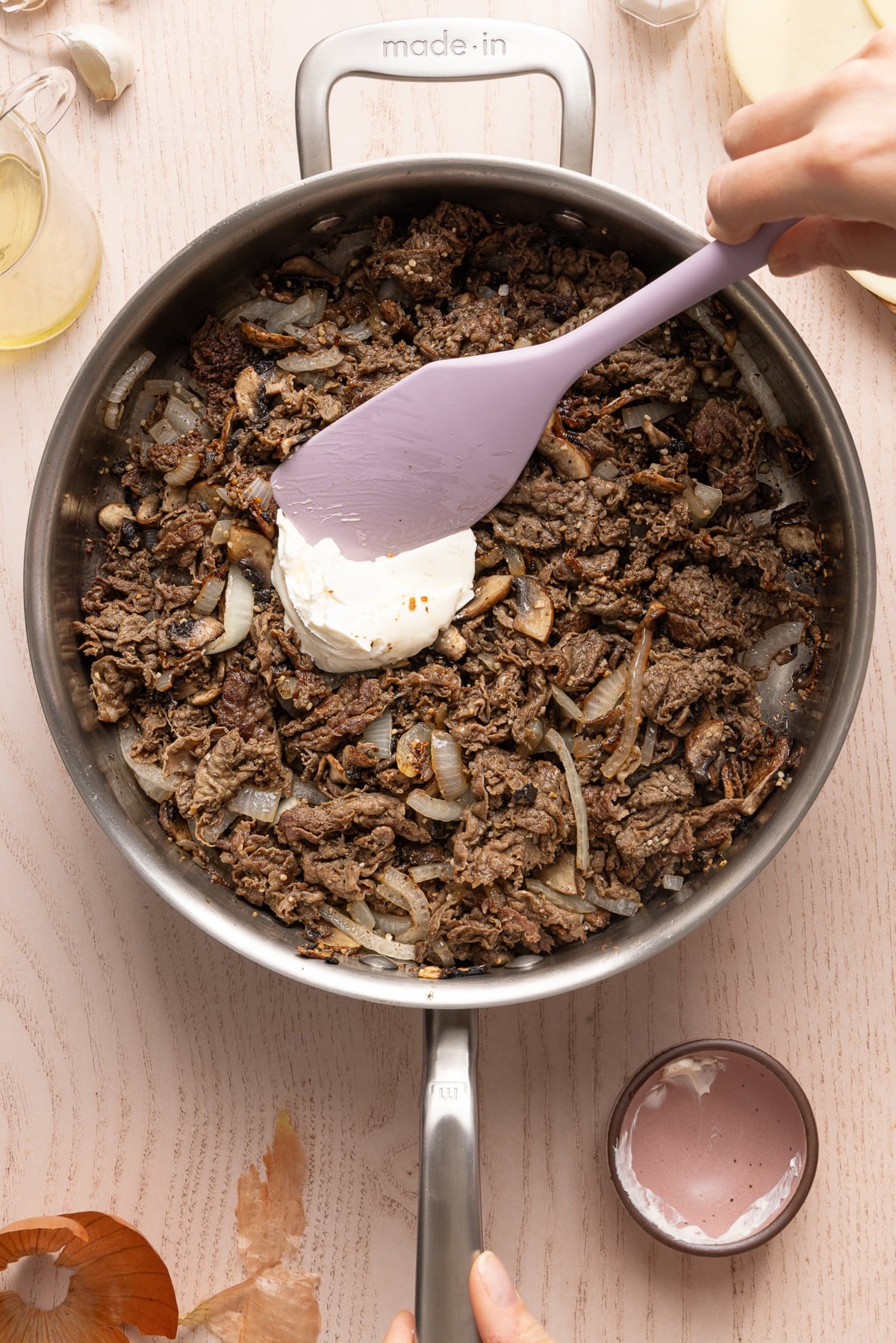 A spatula adds the cream cheese to the pan with the steak and onions mixture.