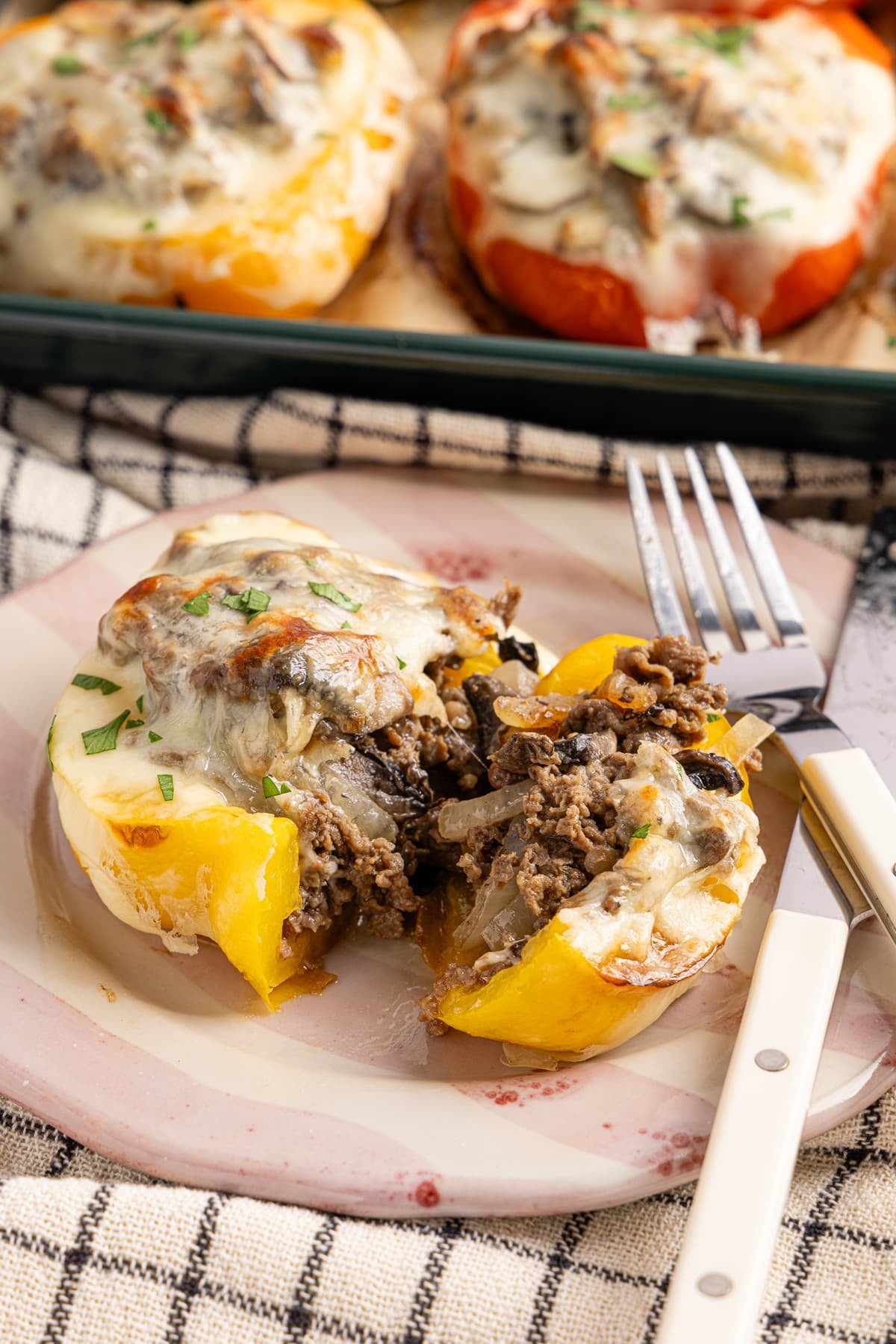 One steak and cheese stuffed pepper cut in half on a plate with a fork.
