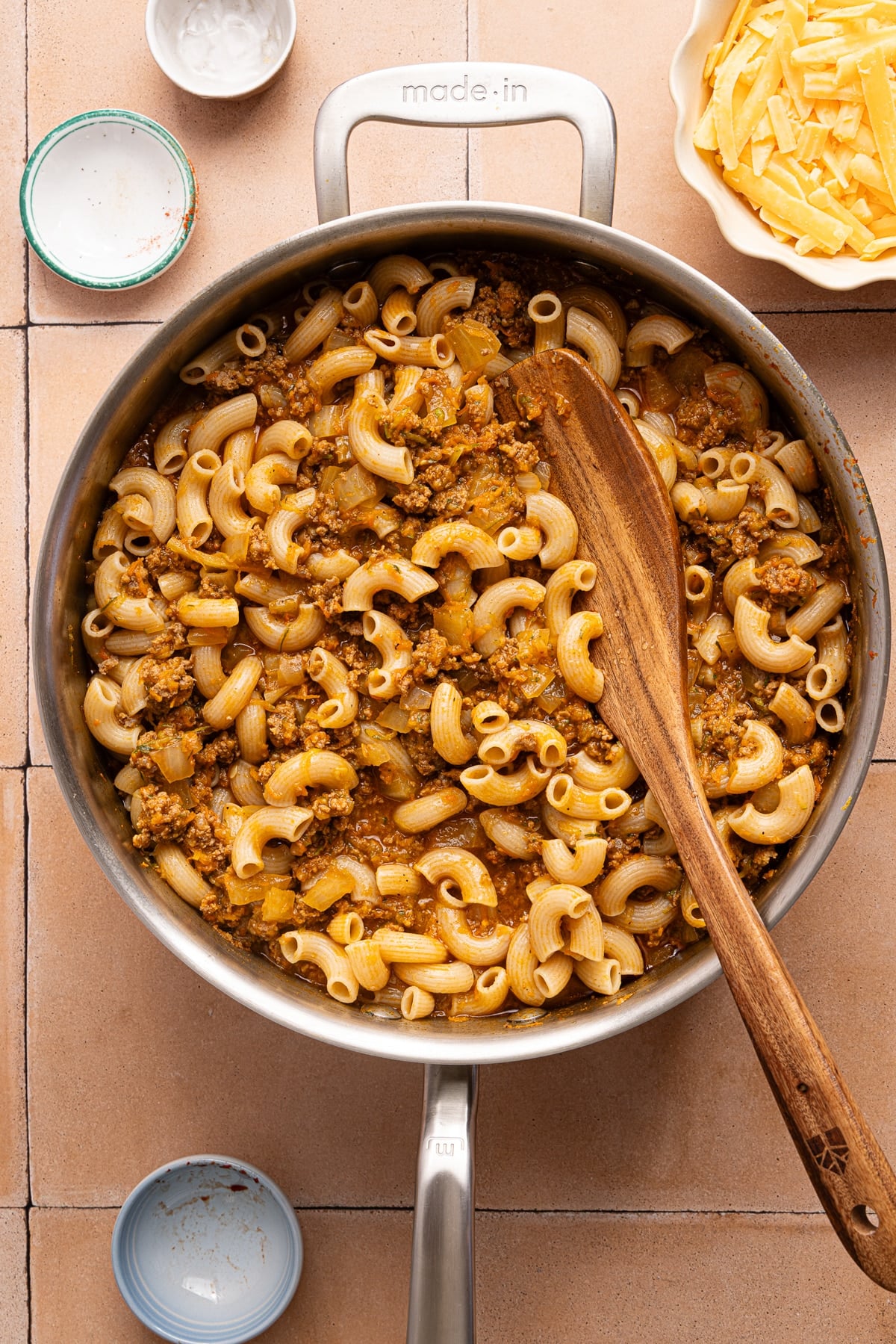 A wooden spoon rests in the pan with the cooked hamburger helper before adding the cheese.