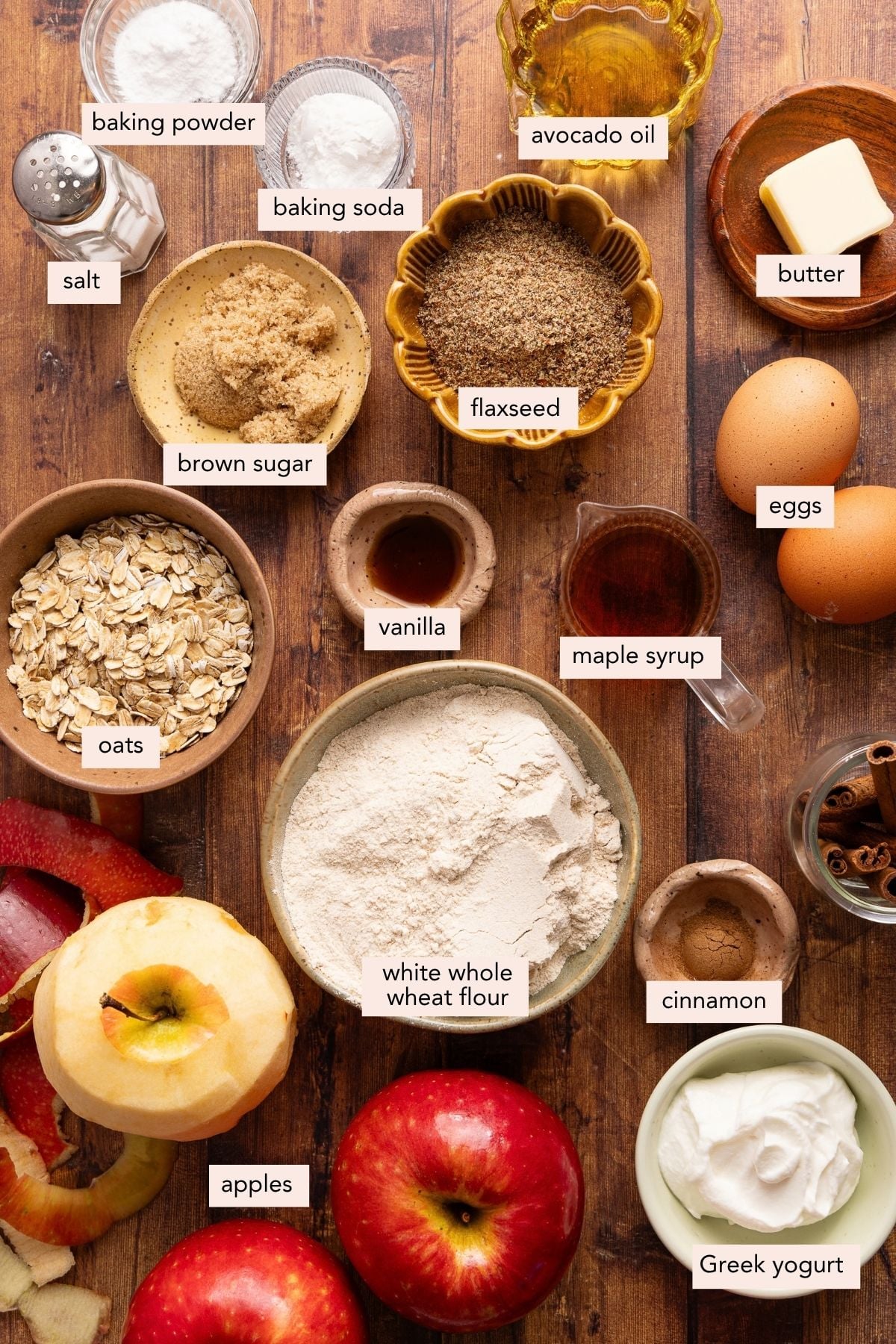 All of the ingredients for apple oatmeal muffins in bowls on a wooden countertop.