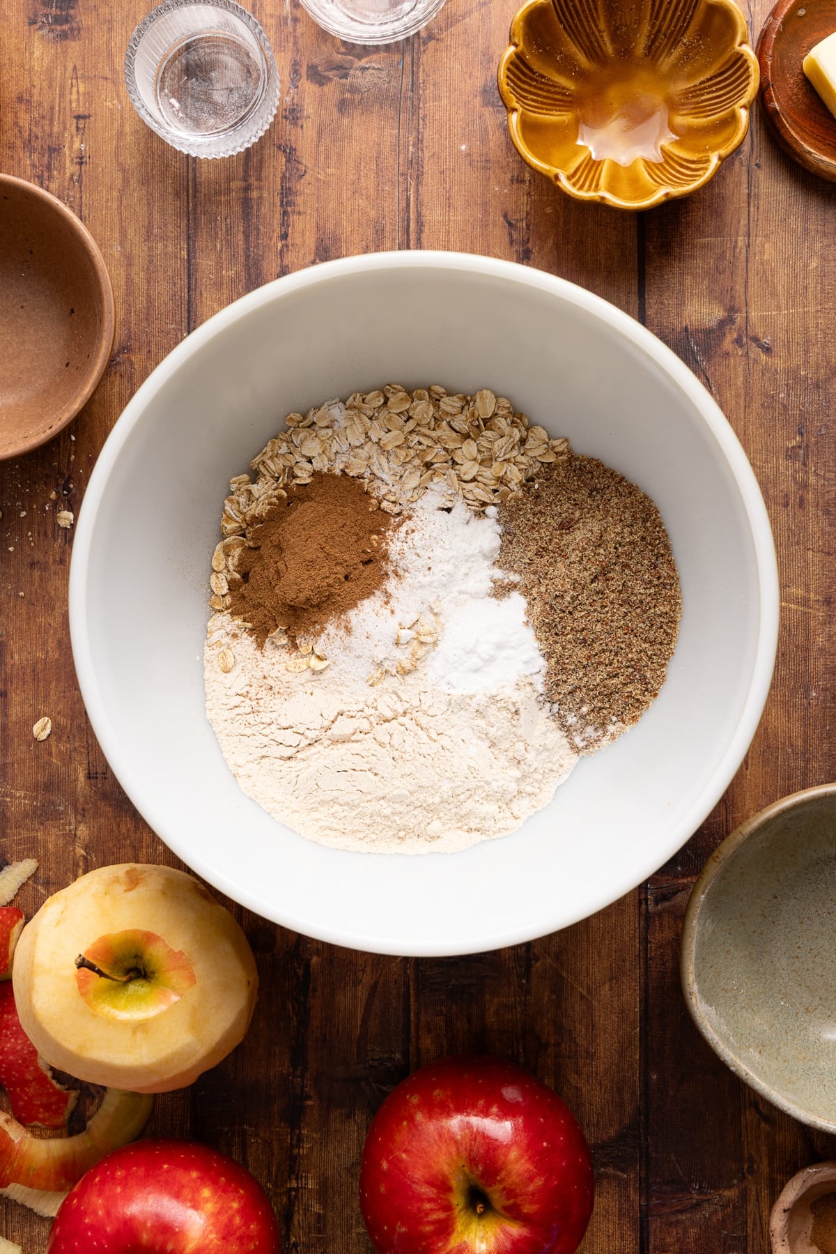 All of the dry ingredients for apple oatmeal muffins in a white bowl on a wooden countertop.