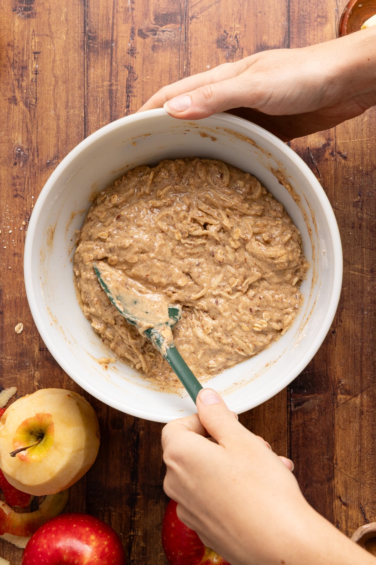 The apple cinnamon oatmeal muffin batter mixed together in a white bowl on a wooden countertop.