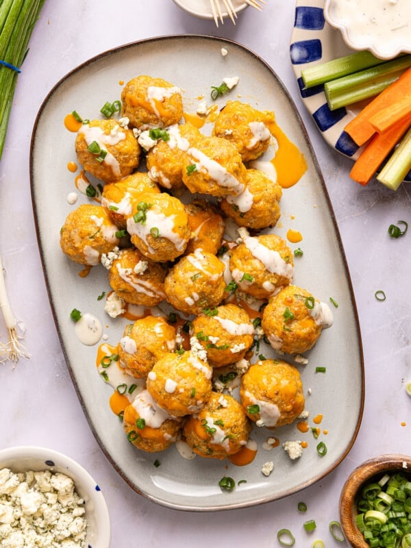 A white serving platter with buffalo chicken meatballs with a drizzle of ranch on top.
