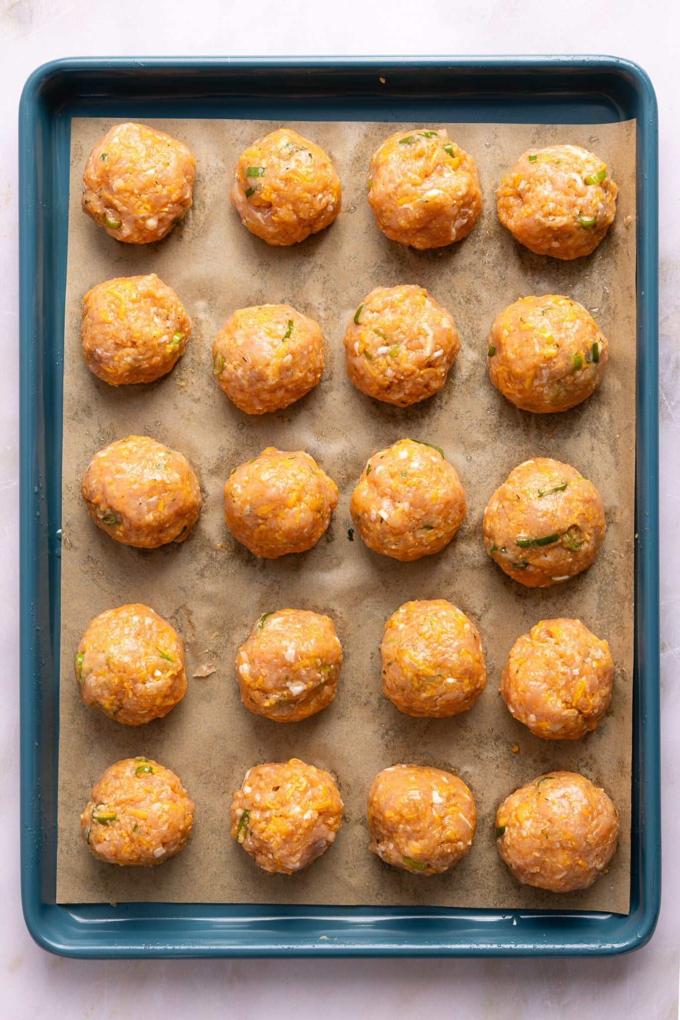 The rolled chicken meatballs on the baking sheet before baking in the oven.