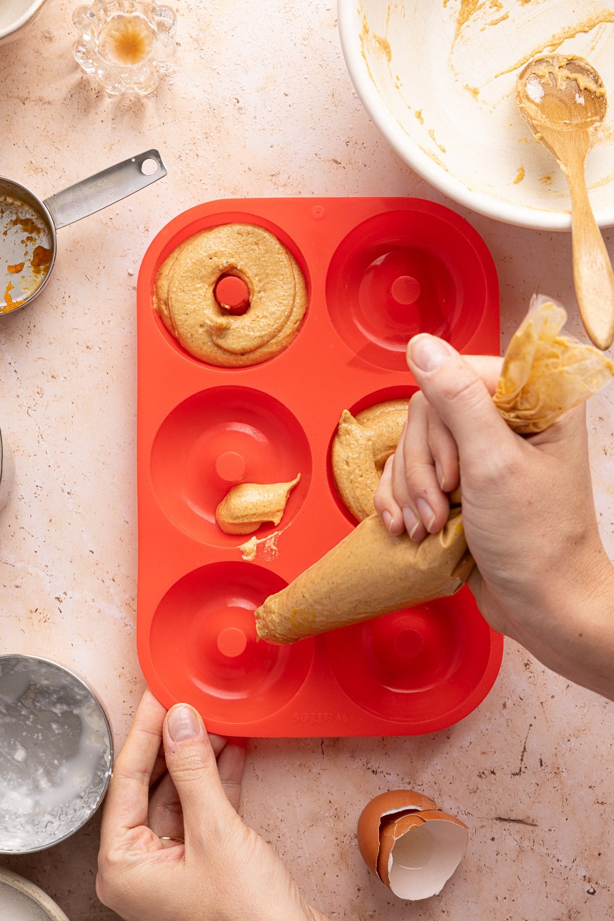 A hand uses a pastry bag to pipe the donut batter into a silicone donut pan.