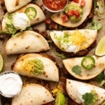 Sheet pan tacos on a baking sheet after baking in the oven with a bowl of salsa and sour cream on the side.