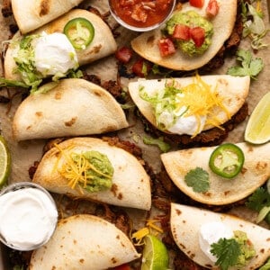 Sheet pan tacos on a baking sheet after baking in the oven with a bowl of salsa and sour cream on the side.