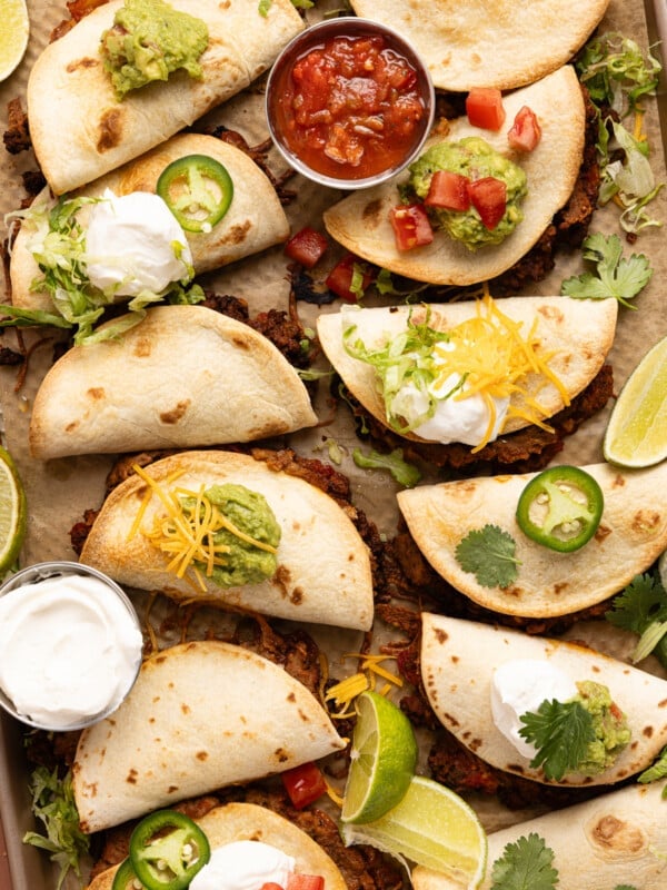 Sheet pan tacos on a baking sheet after baking in the oven with a bowl of salsa and sour cream on the side.