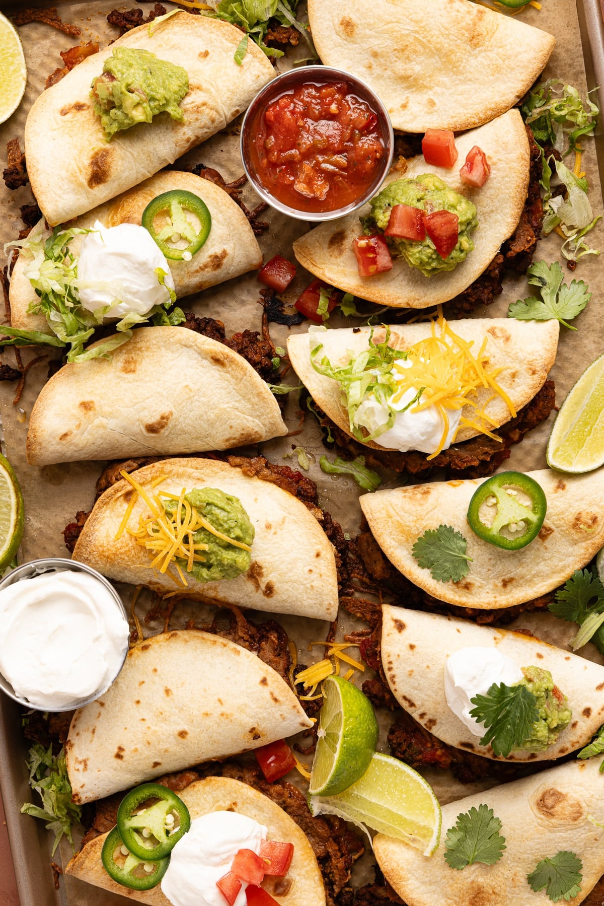 Sheet pan tacos on a baking sheet after baking in the oven with a bowl of salsa and sour cream on the side.