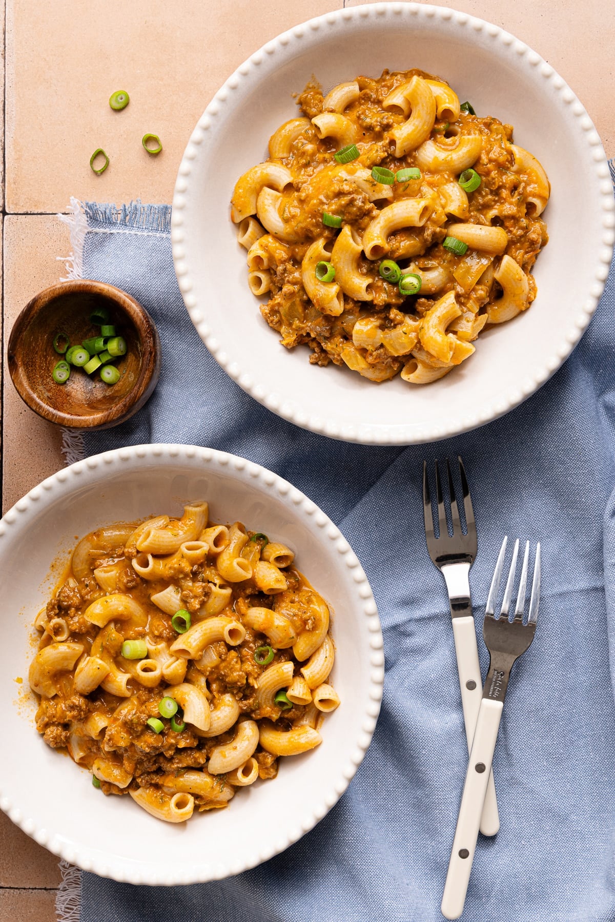 Two bowls of healthy hamburger helper on a tabletop with a blue napkin and forks.