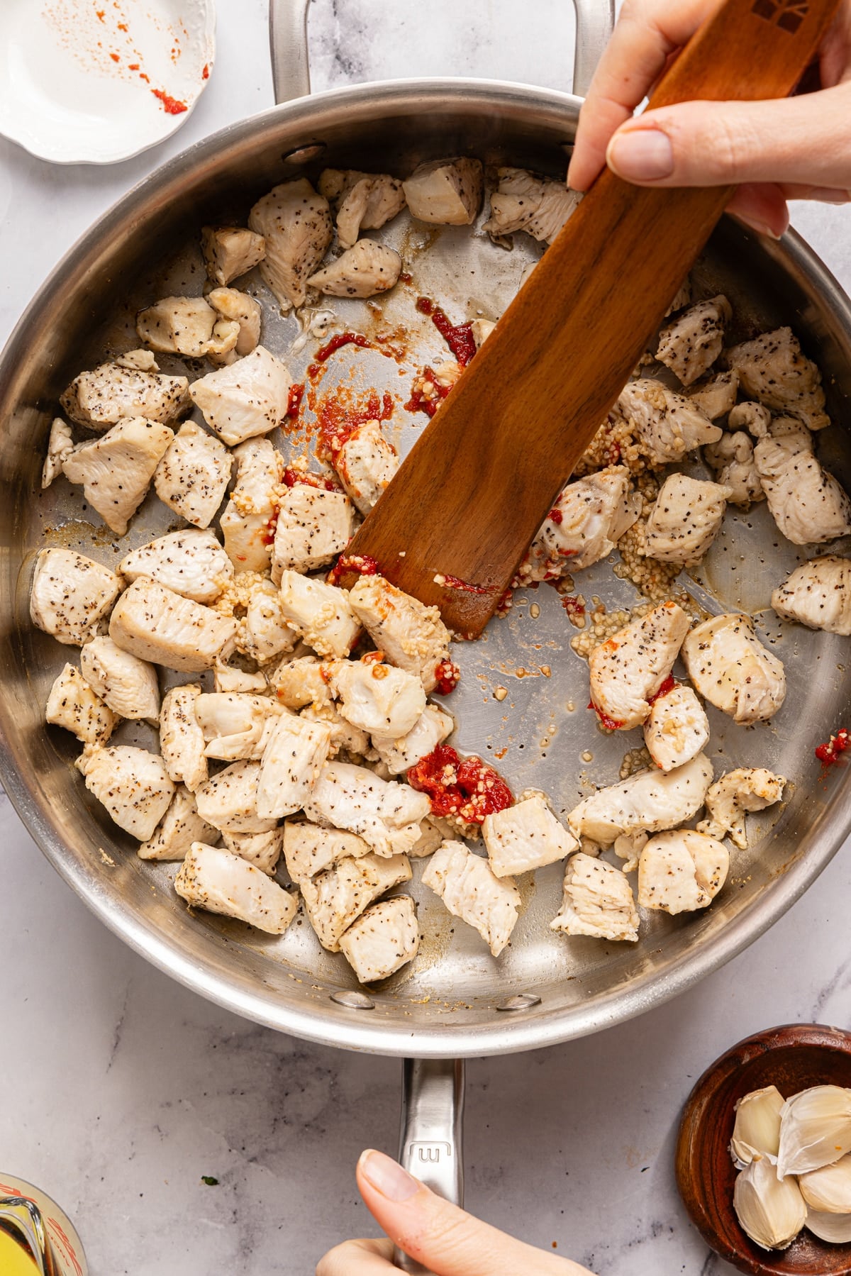 The chicken cooking in the pan with the garlic and tomato paste.