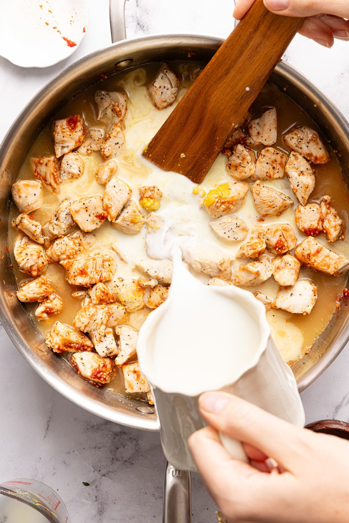 Pouring the milk into the pan with the cooked chicken.