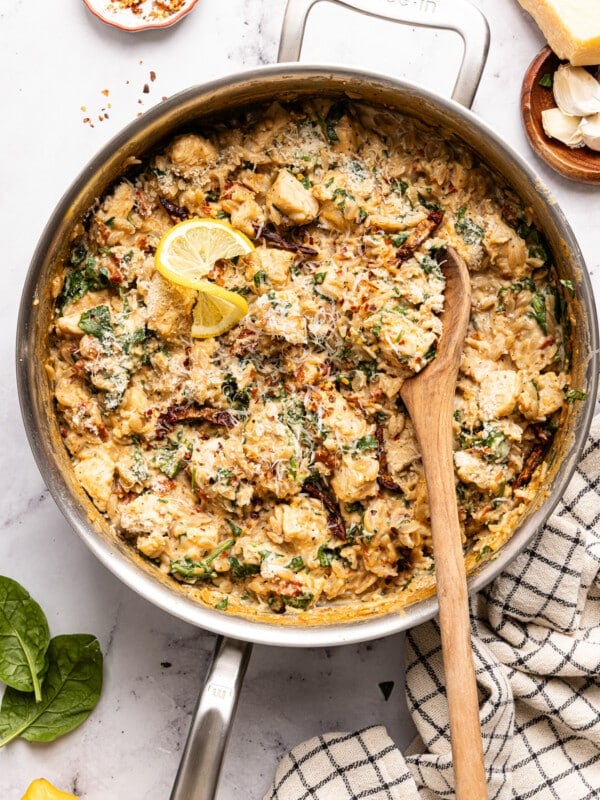 A wooden spoon scoops from the pan of Marry Me Chicken Orzo.