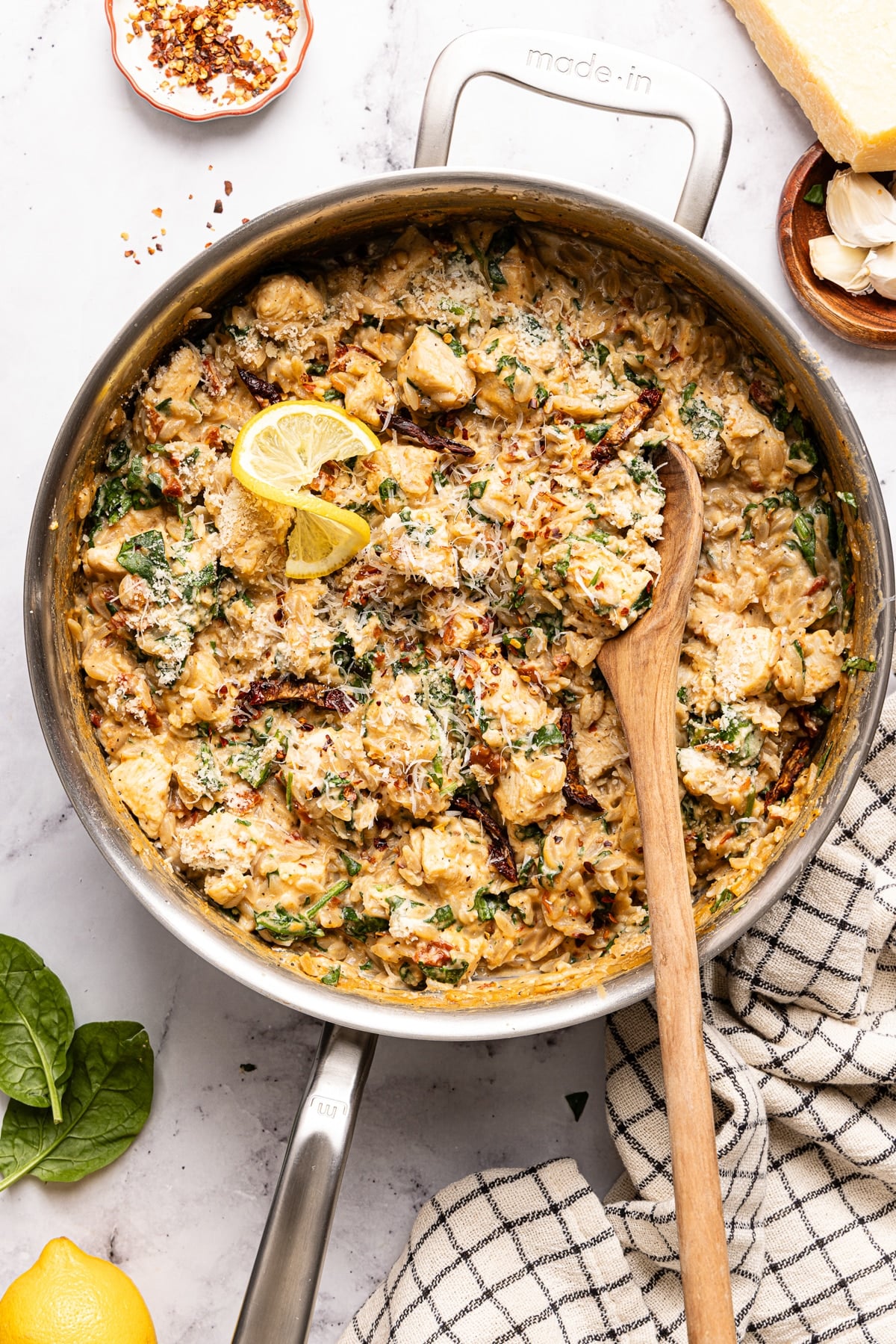 A wooden spoon scoops from the pan of Marry Me Chicken Orzo.
