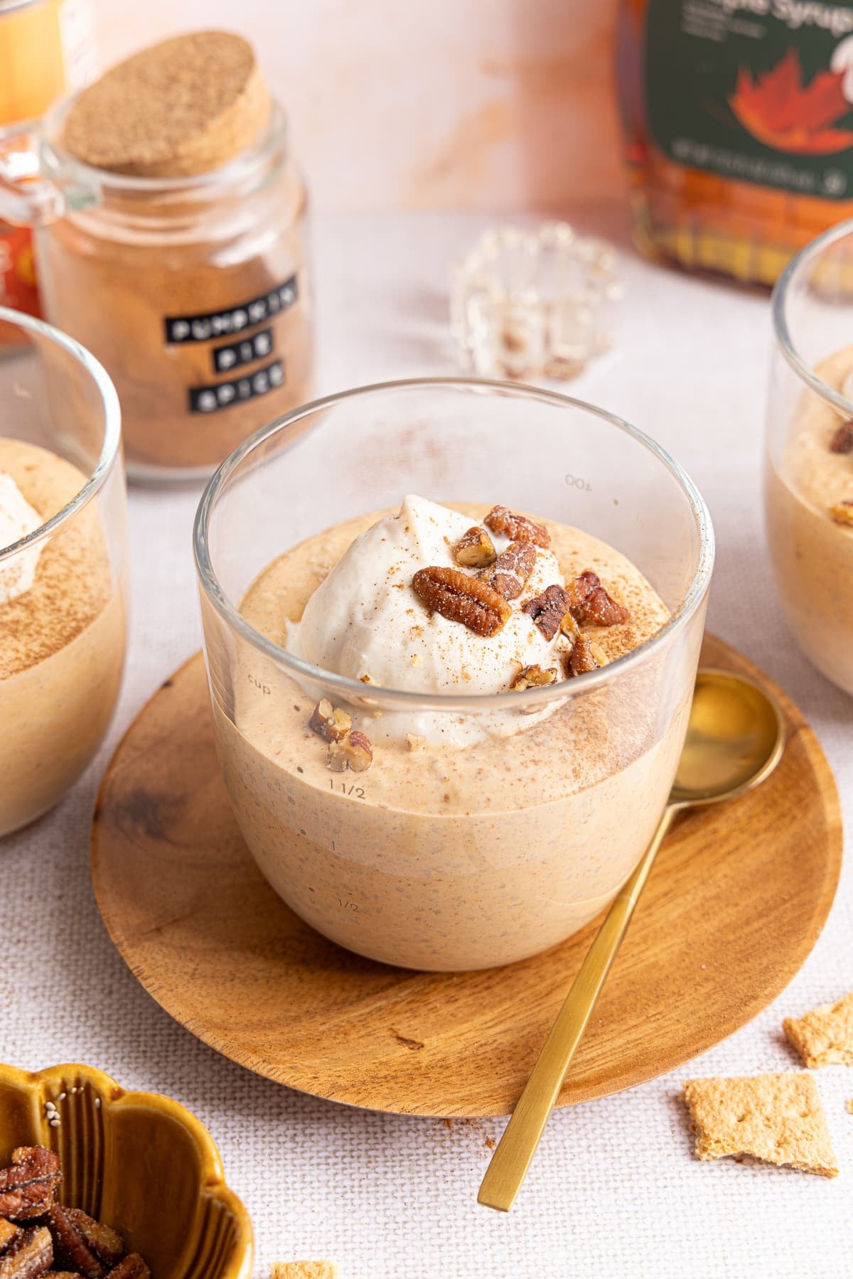 A glass container with the pumpkin chia pudding topped with a dollop of greek yogurt, pecans and crushed graham crackers.