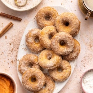 A dozen baked pumpkin cottage cheese donuts on a white serving platter on a countertop.