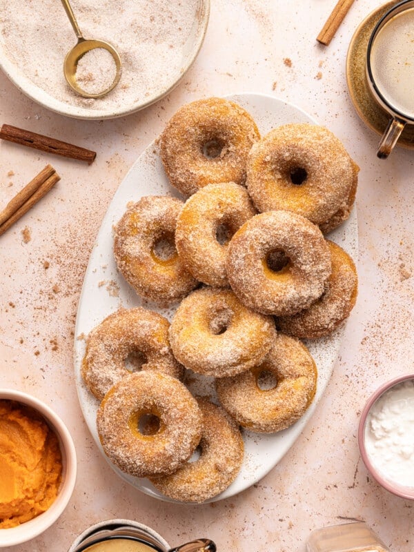 A dozen baked pumpkin cottage cheese donuts on a white serving platter on a countertop.