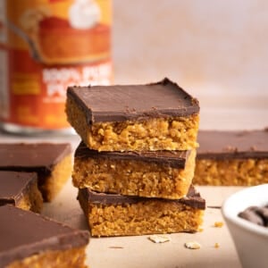 A stack of three No Bake Chocolate and Peanut Butter Pumpkin Oat Bars on a countertop.