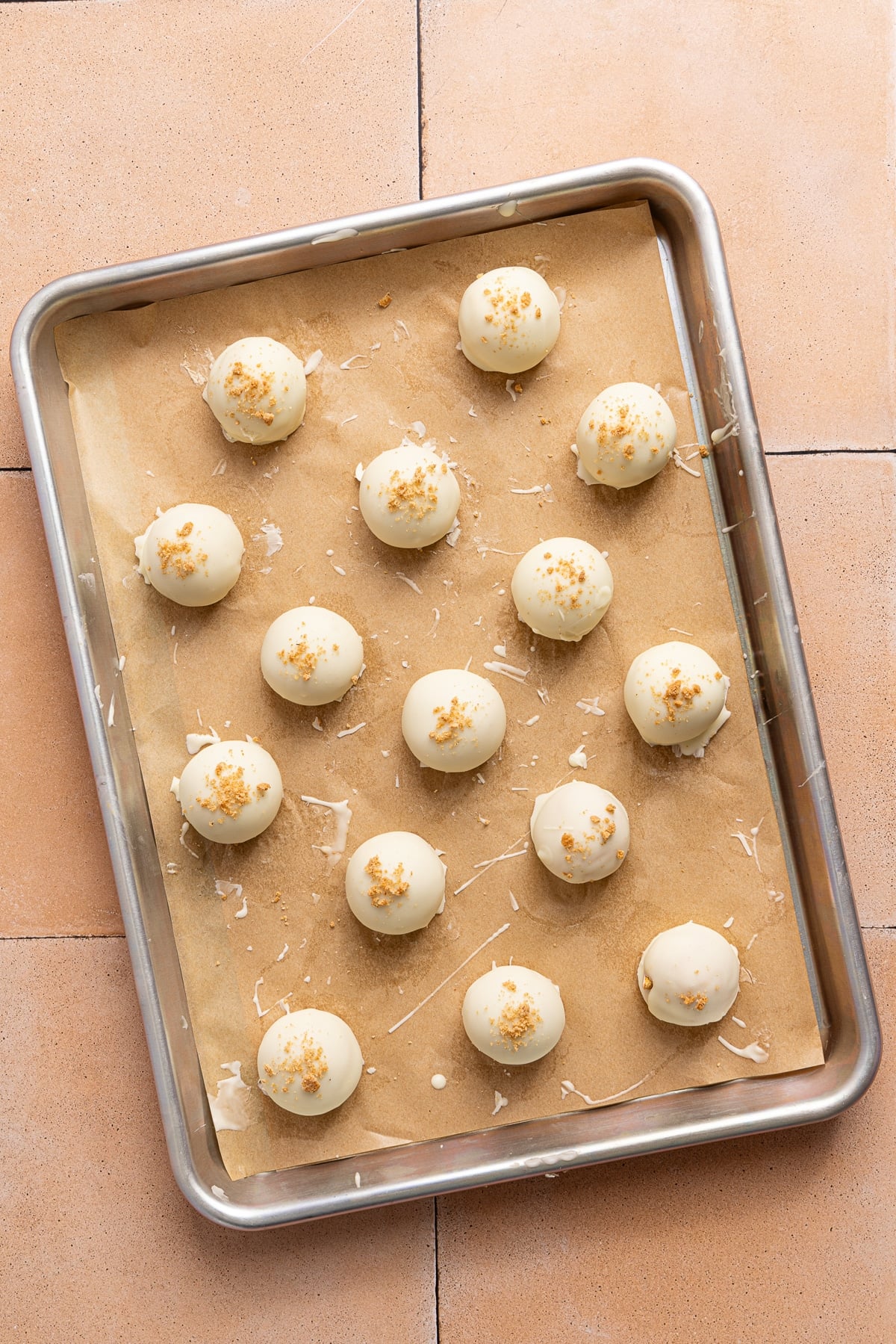 15 white chocolate dipped pumpkin truffles sitting on a sheet pan lined with parchment paper after chilling in the fridge.
