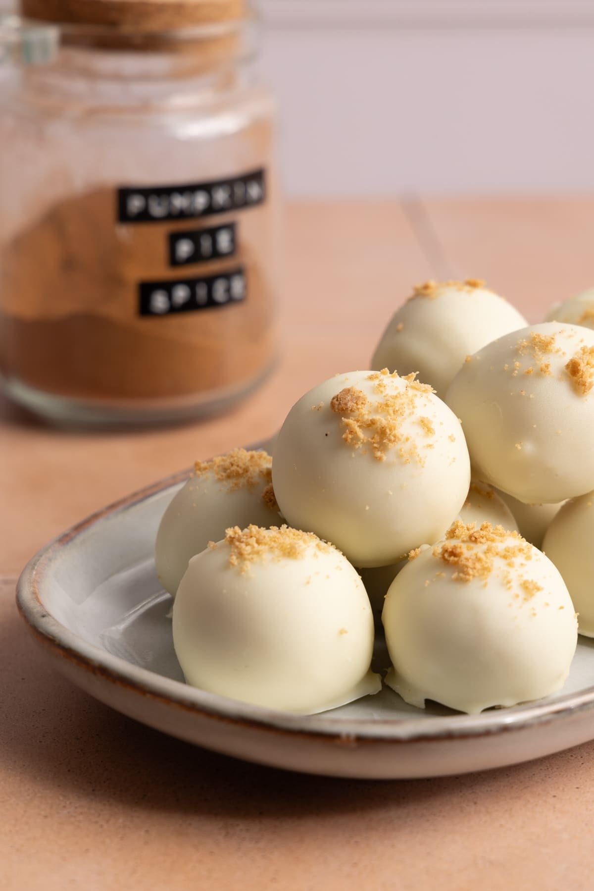 Pumpkin truffles coated in white chocolate sitting on a serving platter on a counter next to a jar of pumpkin pie spice.