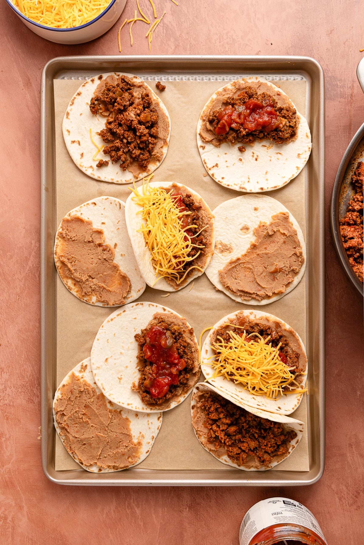 The tacos assembled on the sheet pan with the refried beans, meat, and cheese before baking.