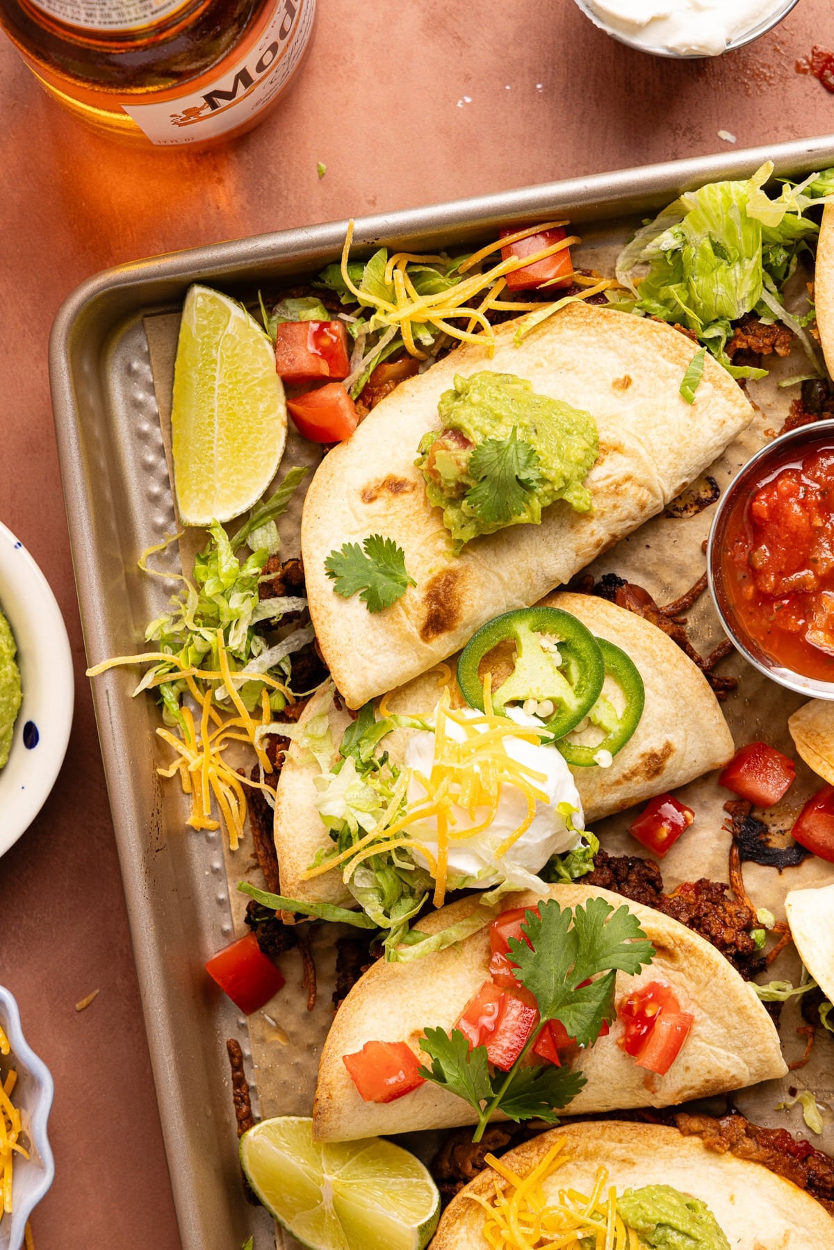 Sheet pan tacos on the baking sheet after baking with sour cream, guacamole, and tomatoes on top.