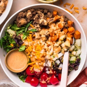 A fork rests in the Sweet Potato Burger Bowls on a countertop with a bowl of pickles on the side.