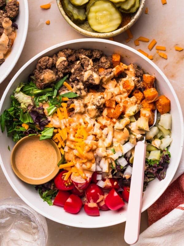 A fork rests in the Sweet Potato Burger Bowls on a countertop with a bowl of pickles on the side.