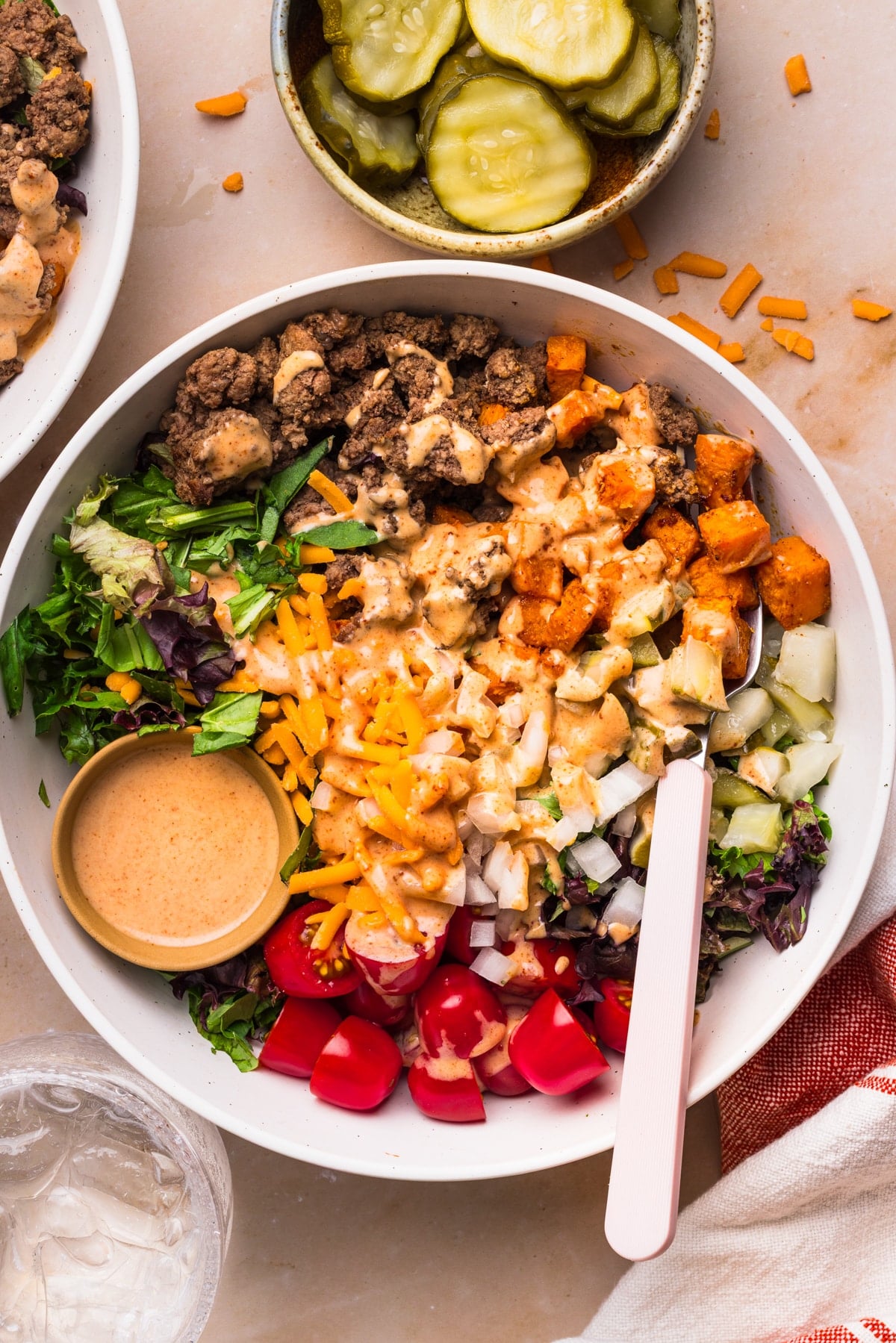 A fork rests in the Sweet Potato Burger Bowls on a countertop with a bowl of pickles on the side.