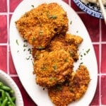 Air fryer chicken cutlets on a white serving platter on a red tile countertop.